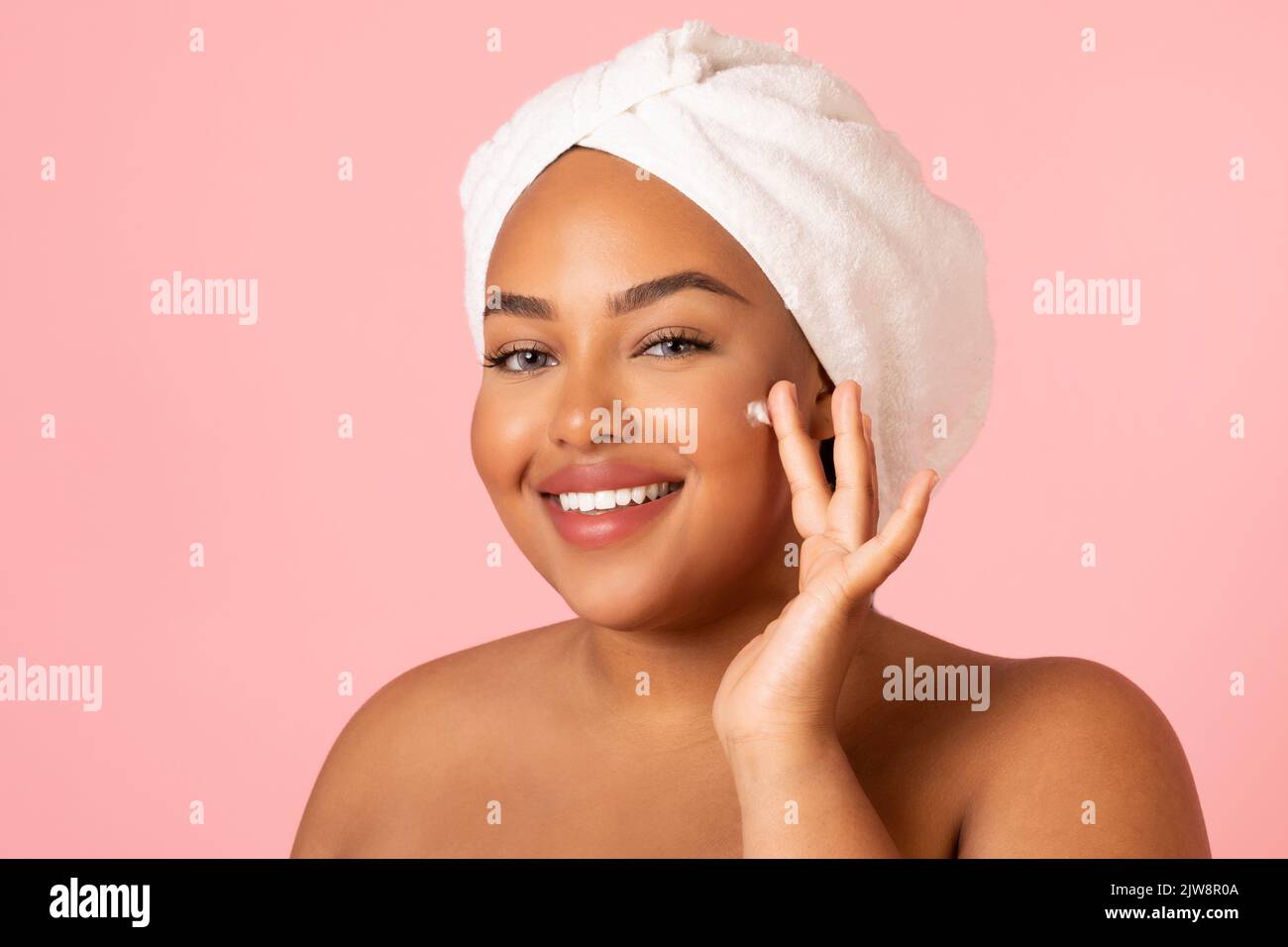 Fettleibige Afroamerikanische Frau, Die Creme Feuchtigkeitsspendend Gesicht, Rosa Hintergrund Stockfoto