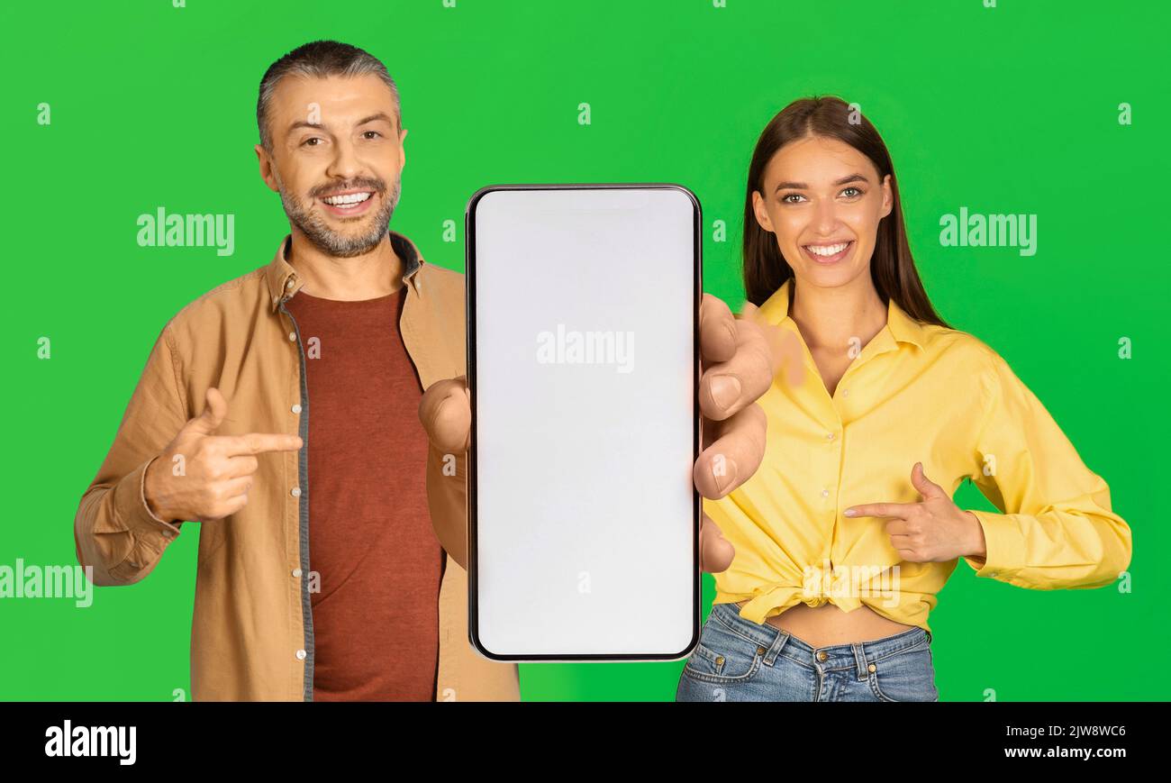 Glücklicher Millennial europäischer Mann und Dame zeigen Finger auf großes Smartphone mit leerem Bildschirm Stockfoto