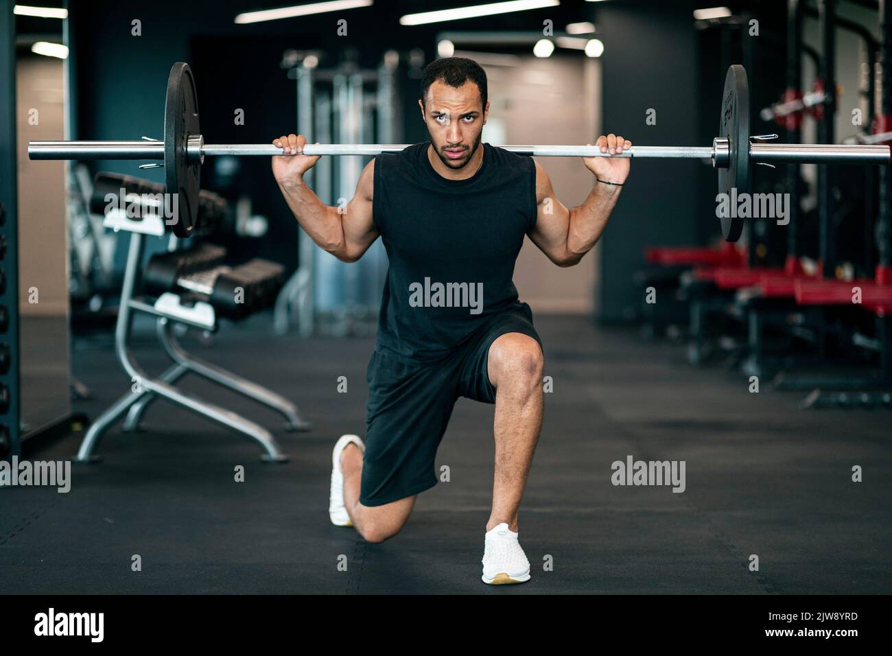 Athletic Young African American Man Making Squats With Heavy Langhantel At Gym Stockfoto