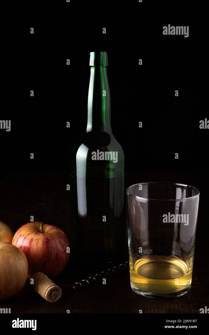 Flasche Cider neben einem Glas mit etwas Cider und ein paar Äpfeln, das Glas mit der normalen Menge, die Cider in der Regel serviert wird. Stockfoto