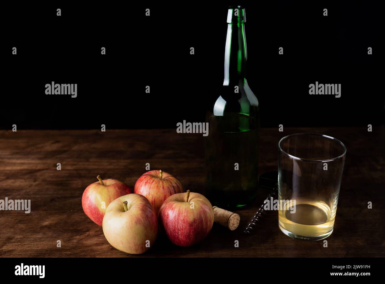 Flasche Cider neben einem Glas mit etwas Cider und ein paar Äpfeln, das Glas mit der normalen Menge, die Cider in der Regel serviert wird. Stockfoto