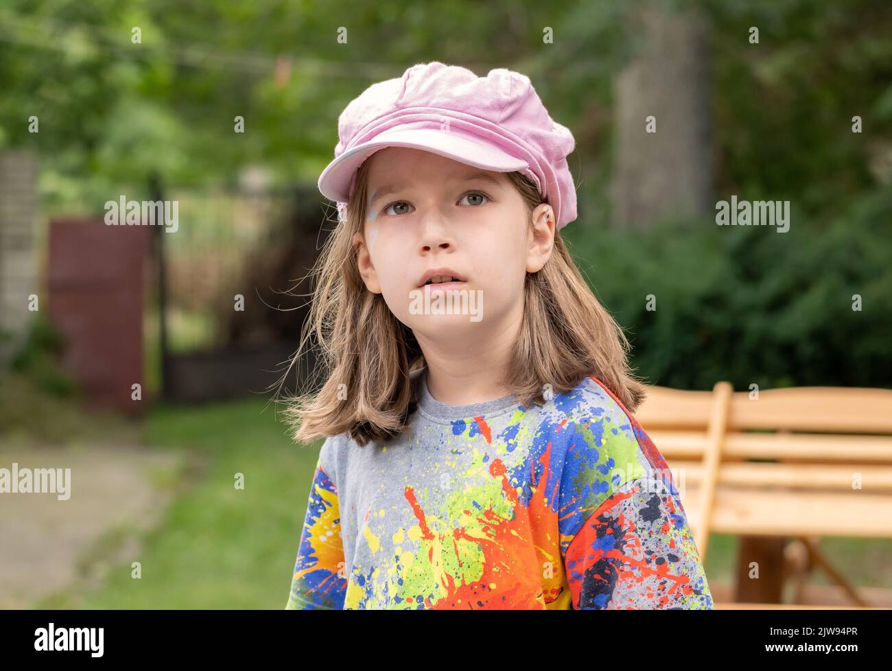 Mädchen im Schulalter, Kinderkünstlerin in einem Lackspritzer-Shirt mit Farbmarkierungen auf dem Gesichtsporträt, Nahaufnahme. Selbstbewusster Künstler, Kind aus nächster Nähe, eine Person, blu Stockfoto
