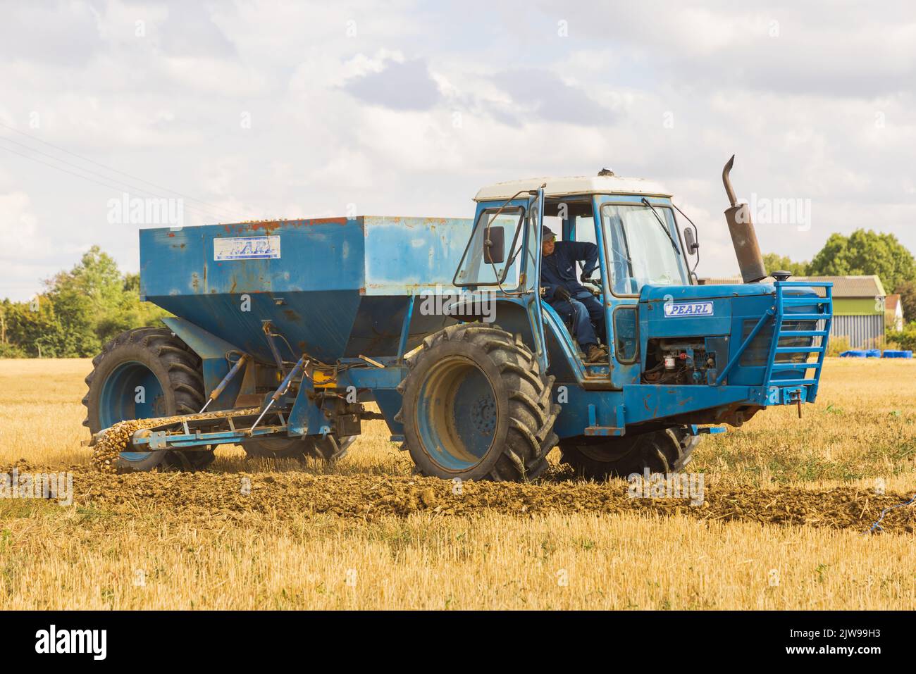 Mann in einem Traktor, der Schindel in einen neu gegrabenen Entwässerungsgraben abgibt. Stockfoto