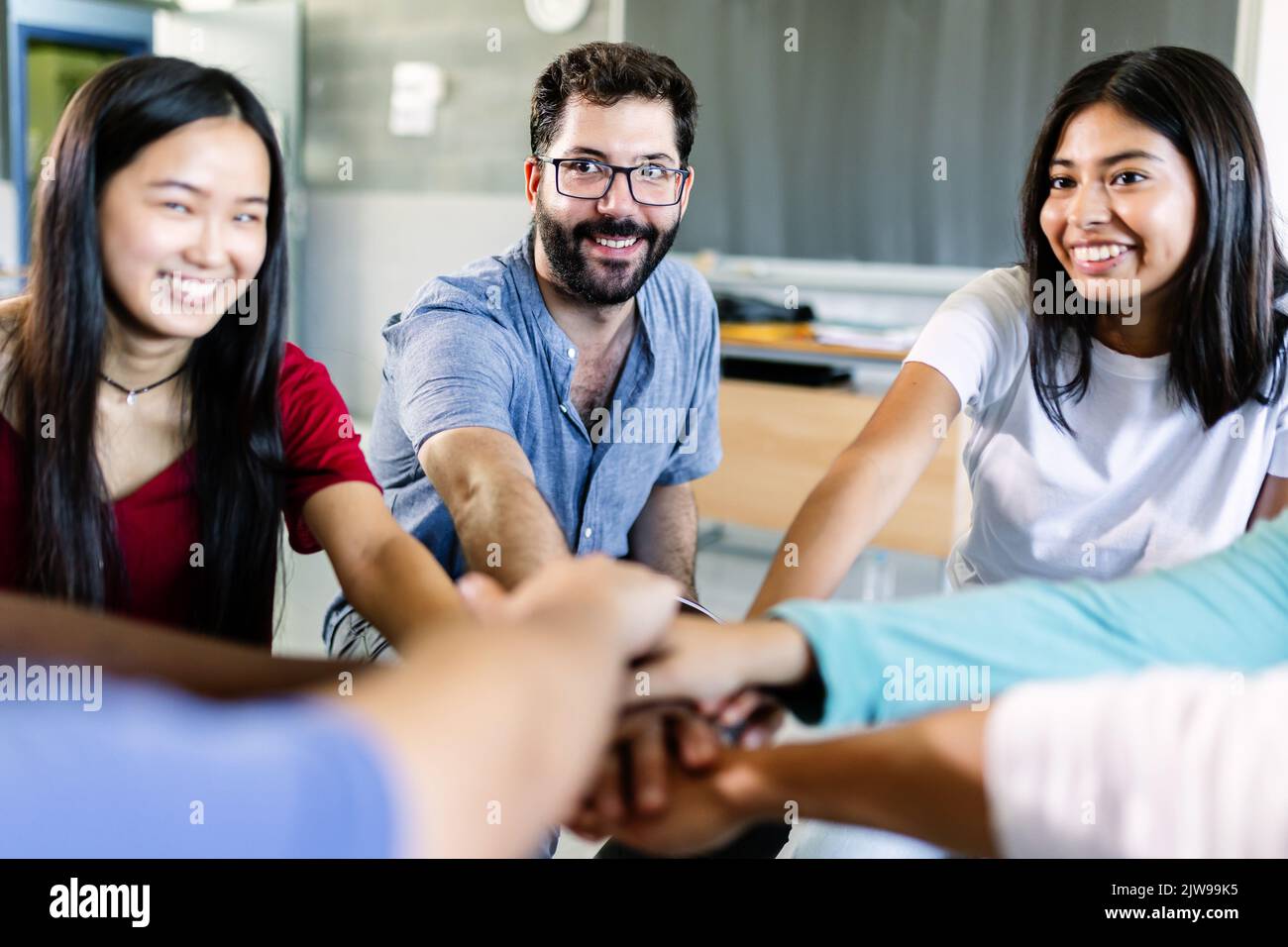 Junge, vielfältige Gruppe von Schülern, die im Klassenzimmer Hände mit einem männlichen Lehrer stapeln Stockfoto