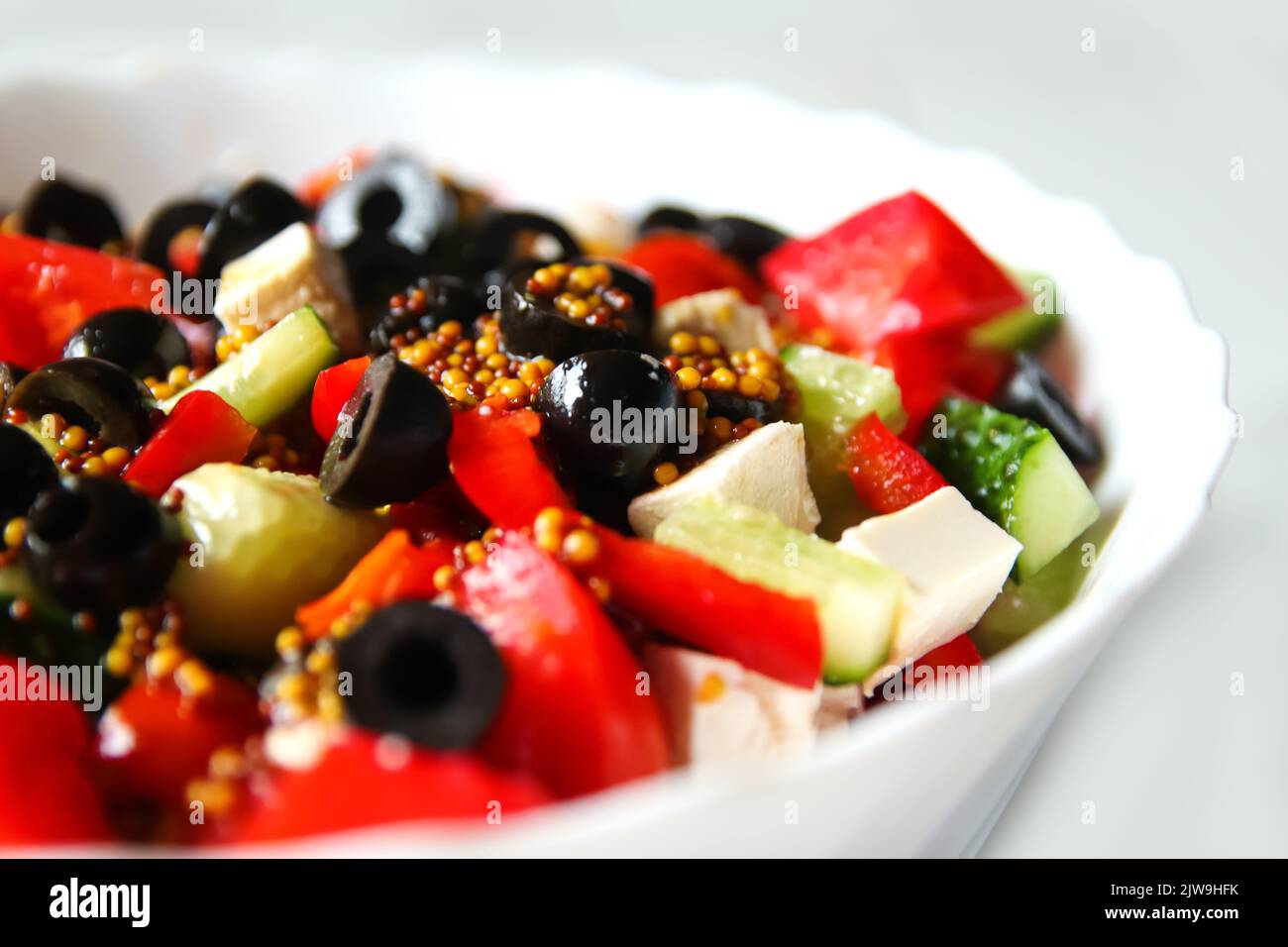 Sommersalat mit Nahaufnahme defokussieren. Klassischer griechischer Salat aus Tomaten, Gurken, rotem Pfeffer, Zwiebeln mit Oliven, Orangen und Feta. Frisches gemischtes Gemüse Stockfoto