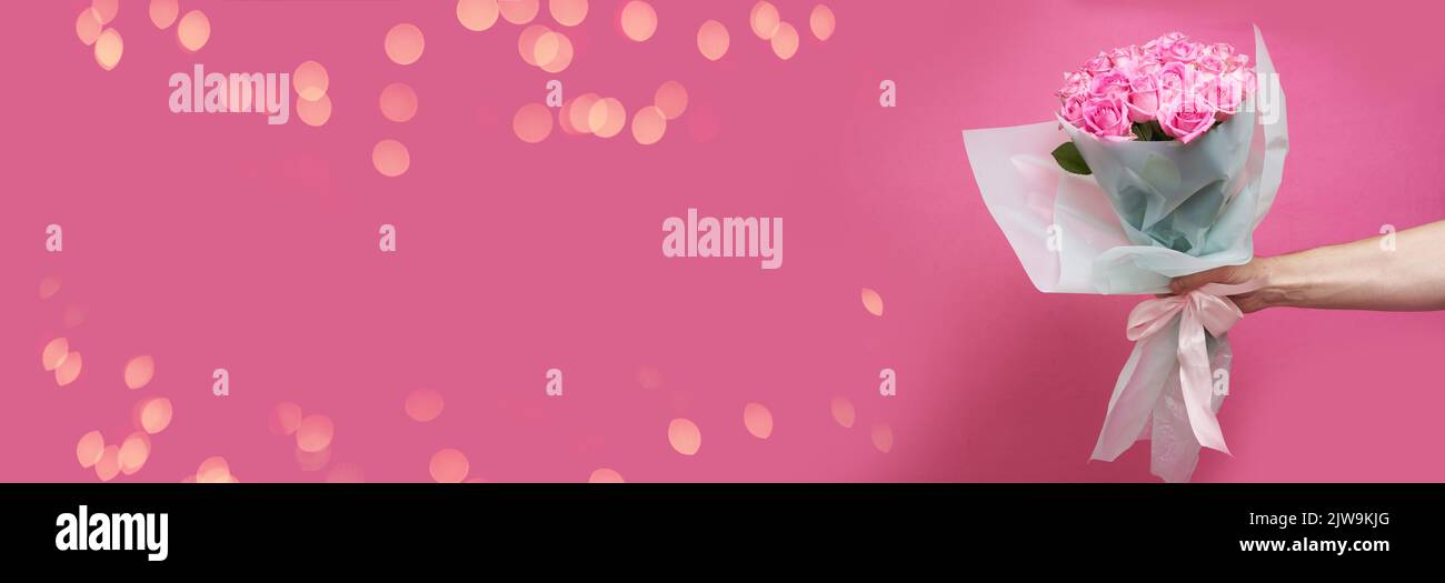 Banner mit Glitzer. Die männliche Hand des Kuriers hält einen Strauß Rosen auf einem rosa Hintergrund aus. Mit Platz zum Kopieren. Hochwertige Fotos Stockfoto