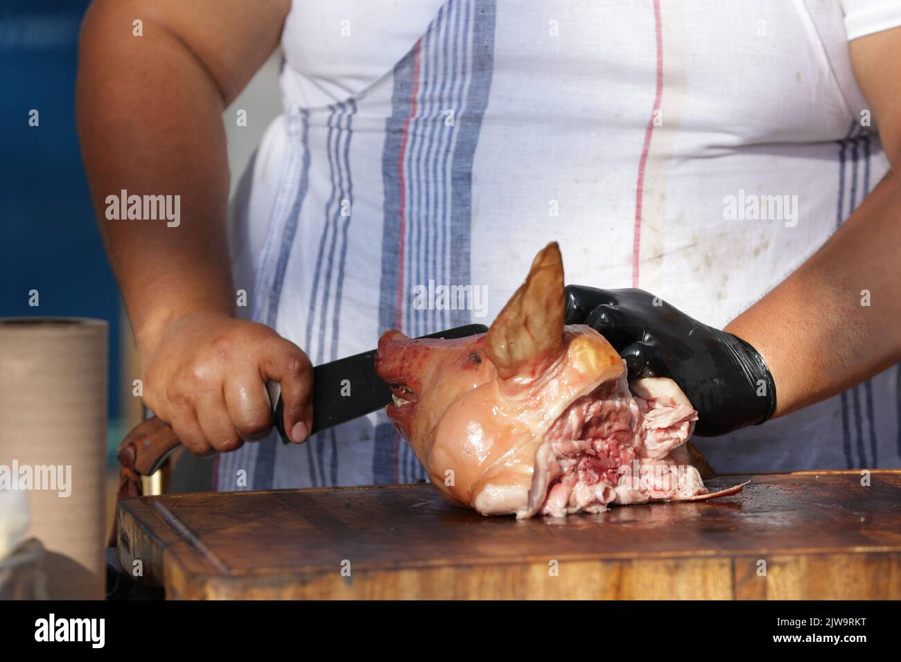 Nahaufnahme eines Metzgers, der einem Spanferkel den Kopf schneidet Stockfoto