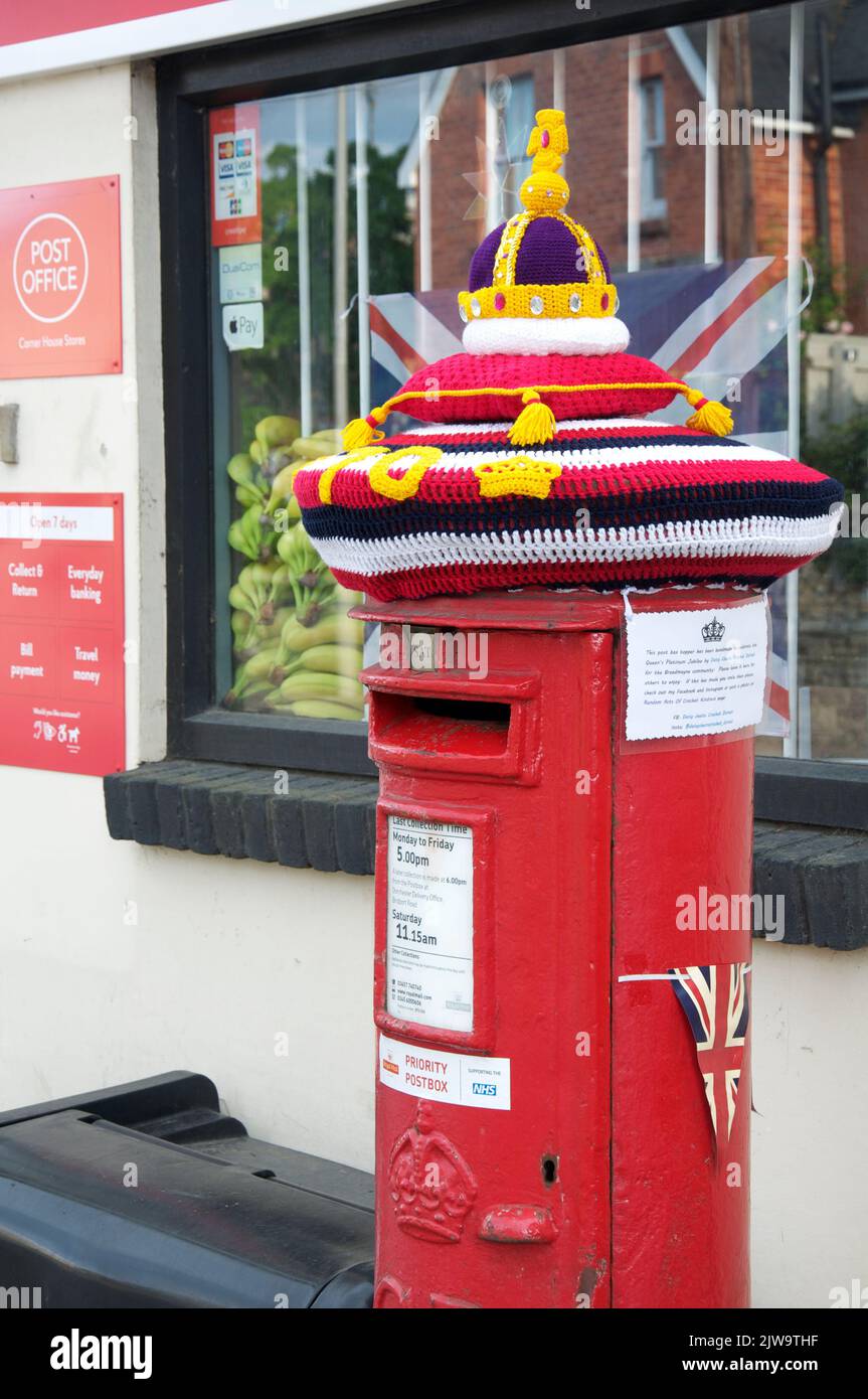 Skurrile bunte handgemachte gestrickte Wollmütze ziert eine traditionelle rote Säulenbox, die das Platin-Jubiläum von Königin Elizabeth II. Feiert England. Stockfoto