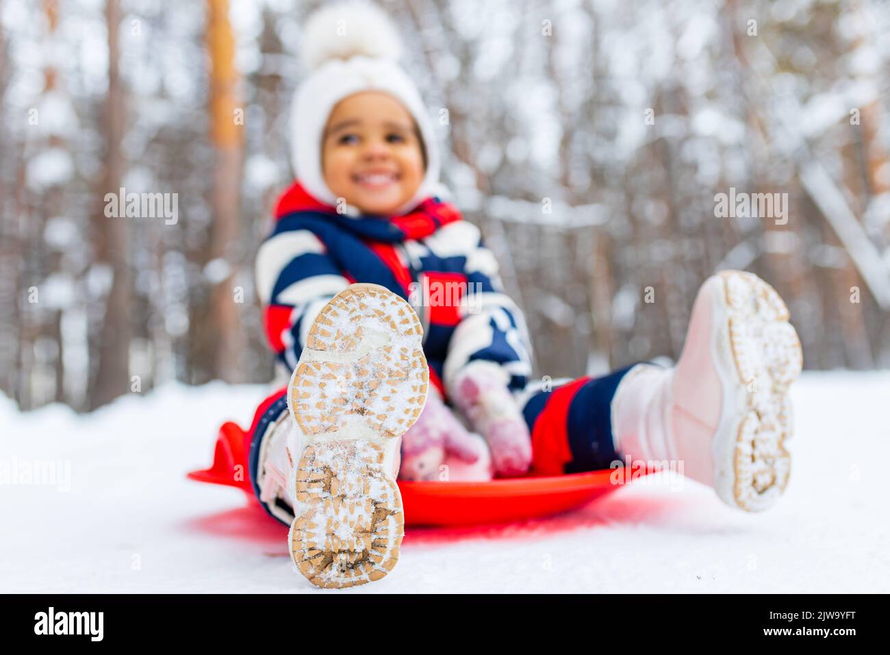 Kleines Mädchen, das Spaß hat und Schlittenfahrten im verschneiten Park macht Stockfoto