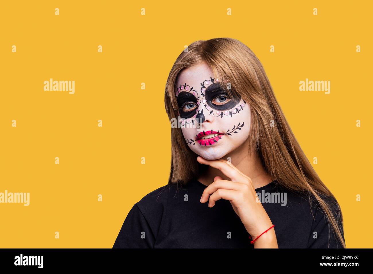 Teenager-Mädchen mit coolen Schädel Make-up mit Rosen auf dem Kopf Blick auf die Kamera in gelben Studio Stockfoto