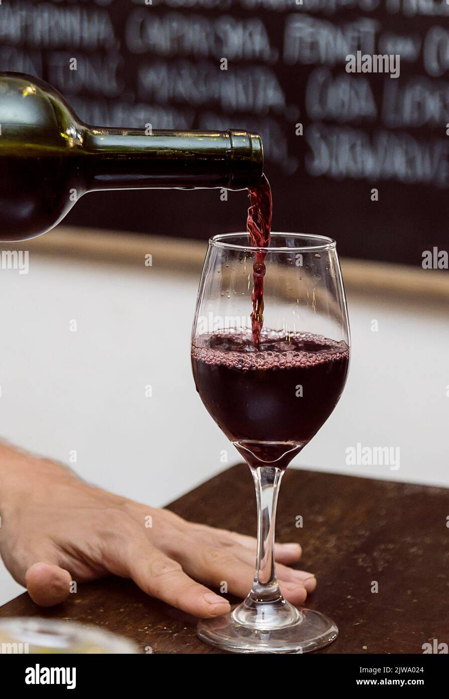 Hand hält eine Flasche Wein und gießt ihn in ein Glas. Atmosphäre im Restaurant Stockfoto