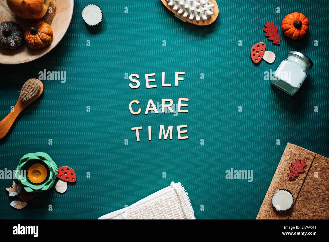 Self-Care Zeit Wort auf grünem Hintergrund flach lag. Selbstpflegetext aus Holz mit Körperpflegeprodukten und Herbstdekor. Stockfoto