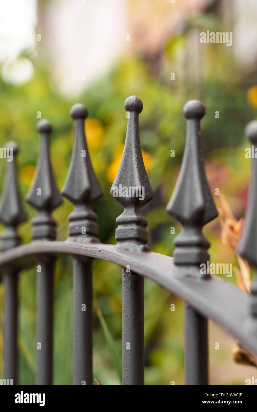 Schmiedeeiserner, spitz zulaufener Metallzaun mit schwarzen Stacheln und linearer Perspektive im grünen Garten. Schutz- und Sicherheitskonzept Stockfoto