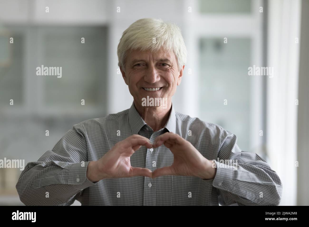 Fröhlicher grauhaariger alter Mann, der das Herz der Hand auf der Brust zeigt Stockfoto