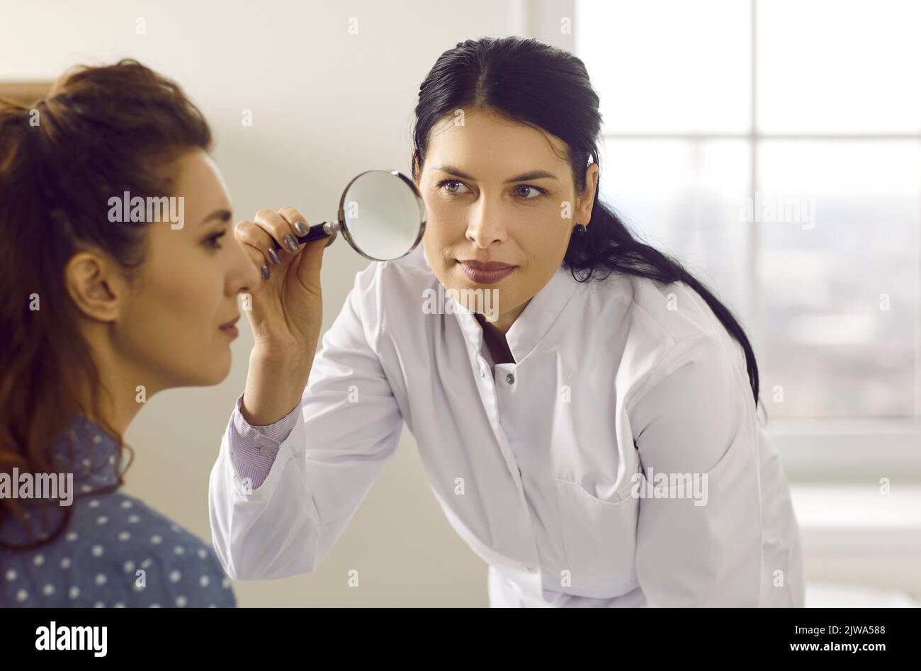 Professioneller Dermatologe mit Lupe und Untersuchung der Haut im Gesicht der Frau Stockfoto