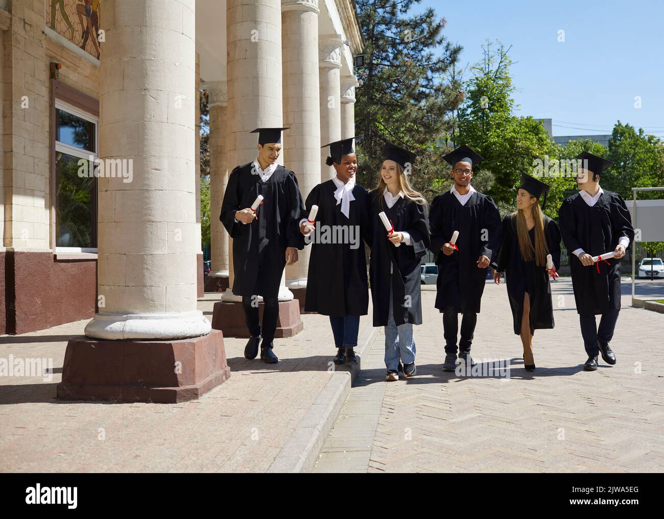 Eine Gruppe von Absolventen spricht, während sie nach der Preisverleihung auf dem College-Campus herumlaufen. Stockfoto