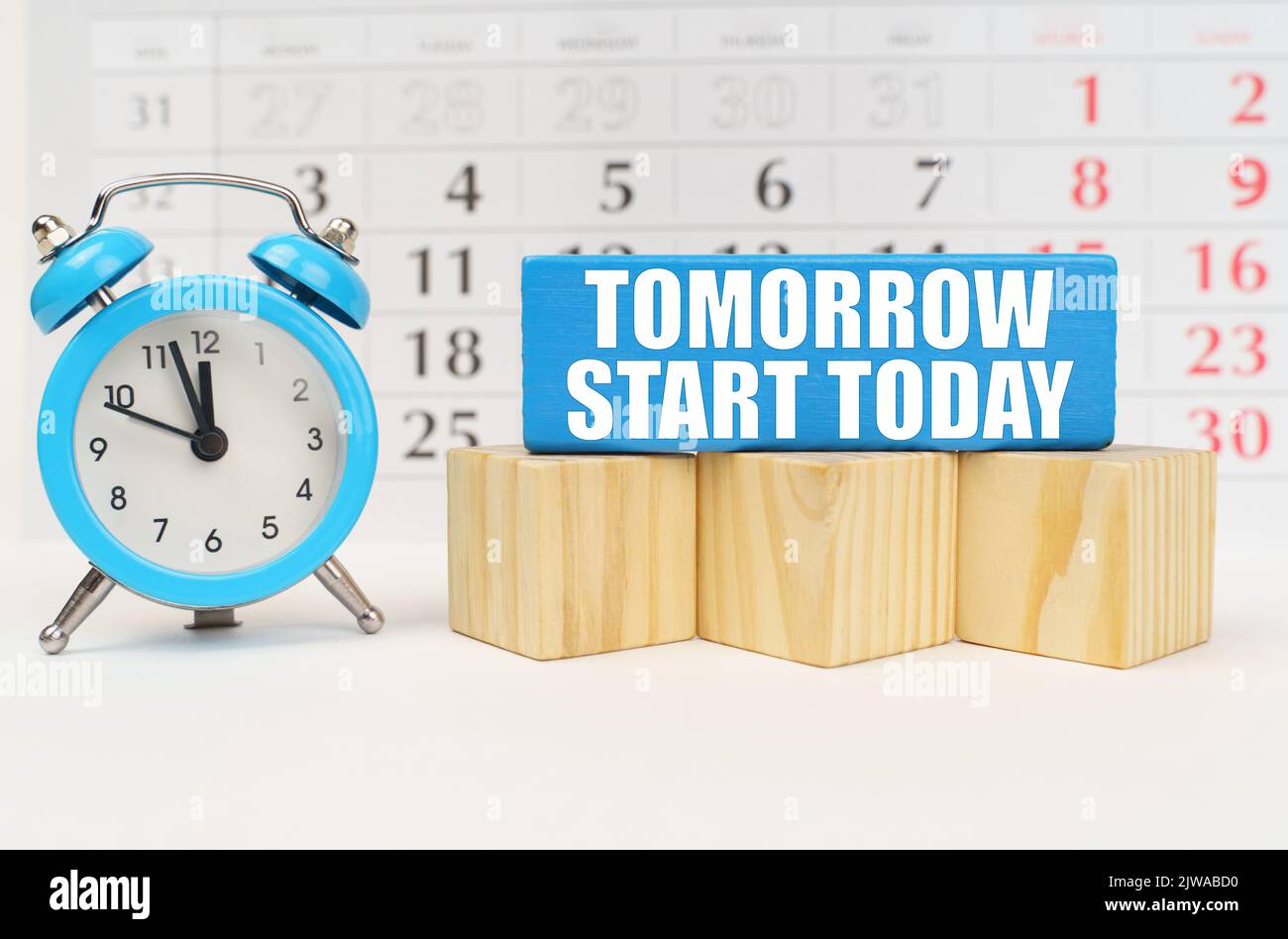 Vor dem Hintergrund des Kalenders, ein Wecker und ein blauer Block mit der Aufschrift - Morgen beginnt heute Stockfoto
