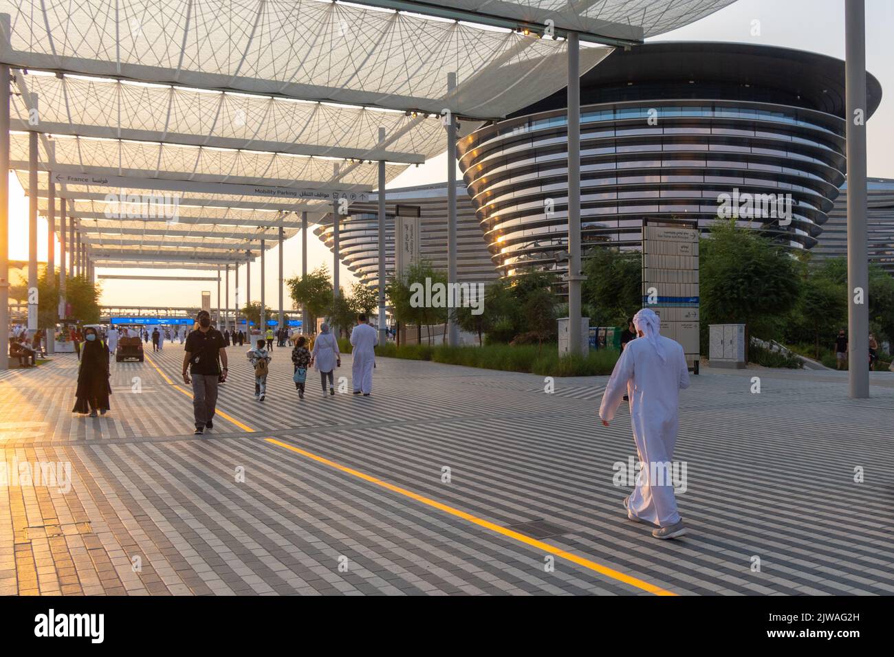 VAE, Dubai - 30. November 2021: Ausstellung EXPO 2020. Menschen gehen zwischen Pavillons entlang. Ausstellungshalle Mobilität in den Abendstrahlen des Sonnenuntergangs. Stockfoto