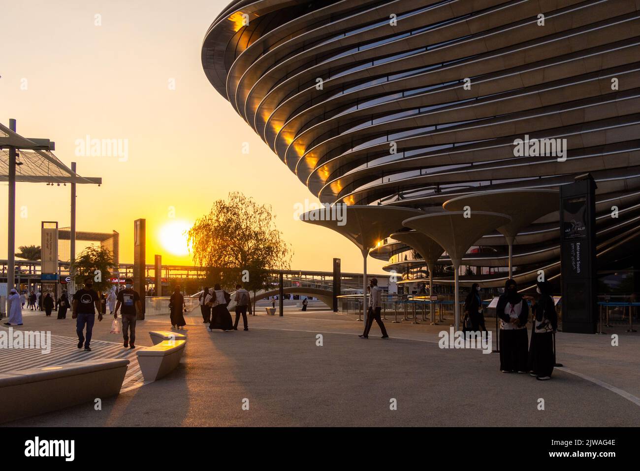 VAE, Dubai - 30. November 2021: Ausstellung EXPO 2020. Menschen gehen zwischen Pavillons entlang. Ausstellungshalle Mobilität in den Abendstrahlen des Sonnenuntergangs. Stockfoto