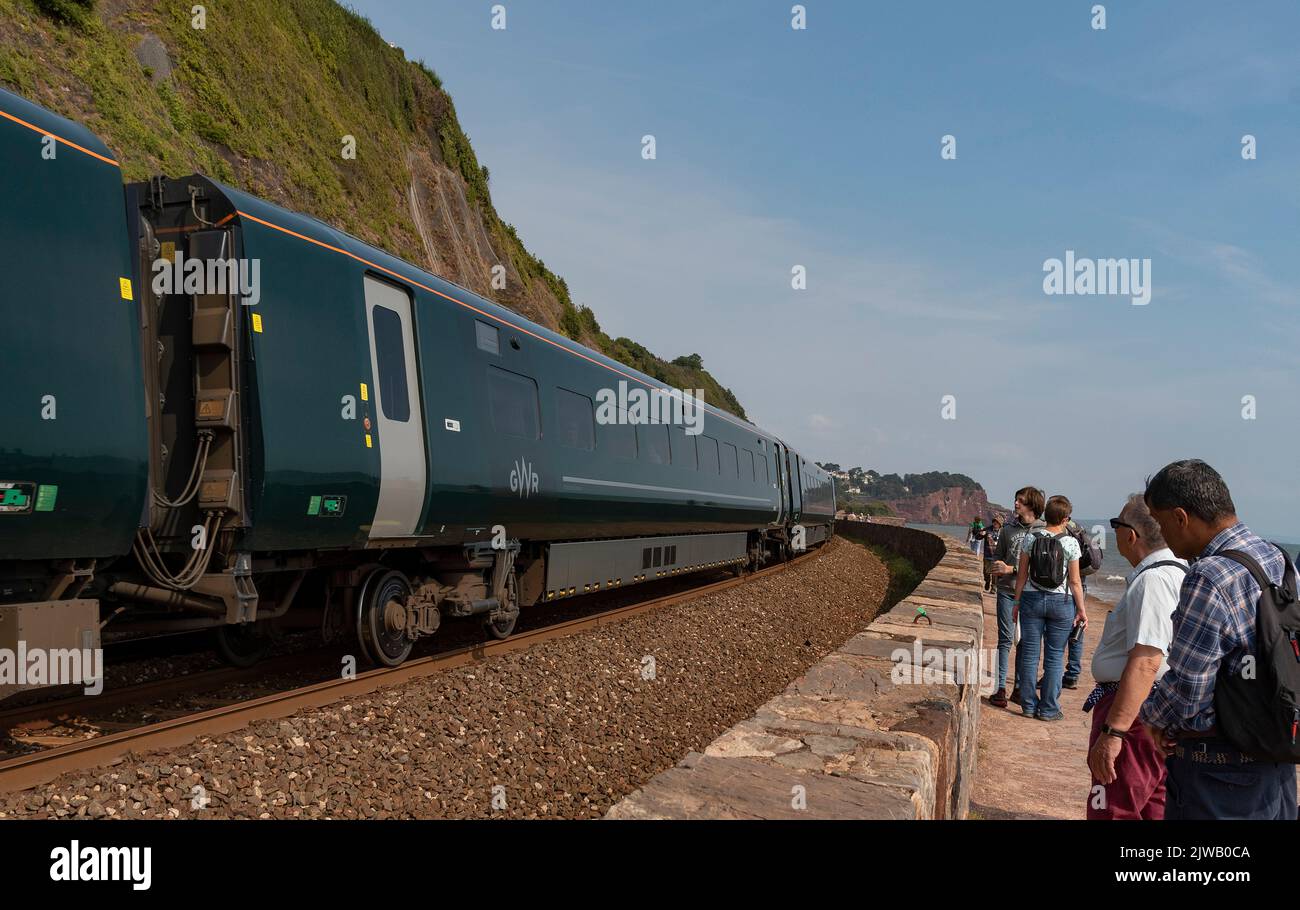 Teignmouth, Devon, England, Großbritannien. 2022. Urlauber halten an der Gleisseite an, um einen Personenzug in Richtung Teignmouth an der Südwestküste zu sehen. Stockfoto