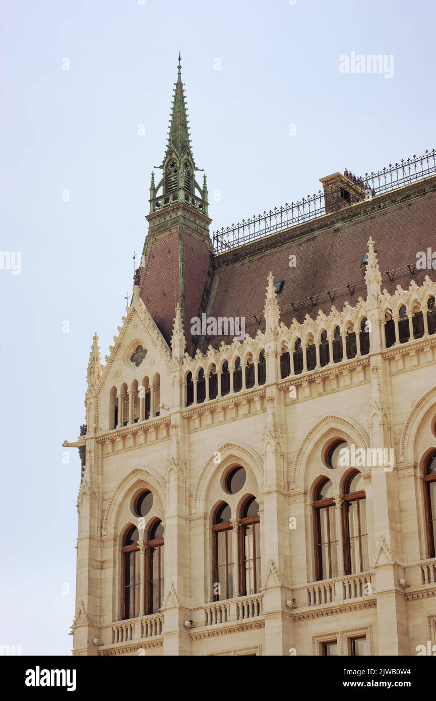 Dies ist ein Teil des Parlamentshauses in Budapest, Ungarn. Sie sehen einen hohen Turm und viele runde und gewölbte Fenster mit einem roten Dach. Stockfoto