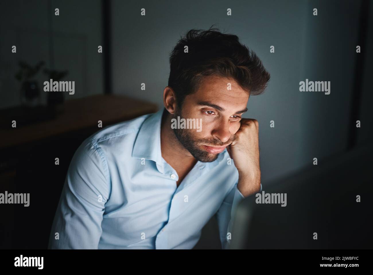 Die Arbeit wird ziemlich monoton. Ein junger Geschäftsmann, der sich langweilen muss, während er spät in einem Büro arbeitet. Stockfoto