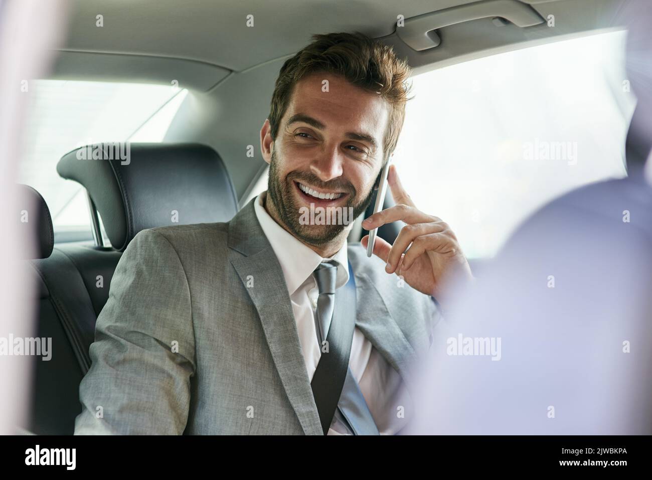 Ein hübscher junger Geschäftsmann, der auf dem Rücksitz eines Autos auf einem Mobiltelefon spricht. Stockfoto
