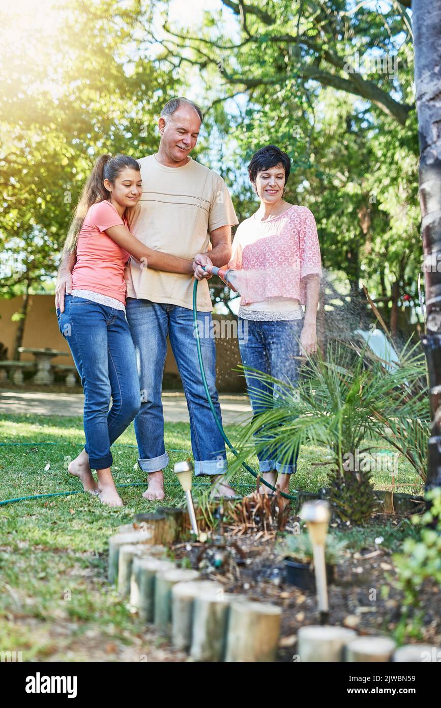 Sie sind eine Familie von grünen Fingern. Eine Familie, die einen Garten mit einem Schlauch bewässert. Stockfoto