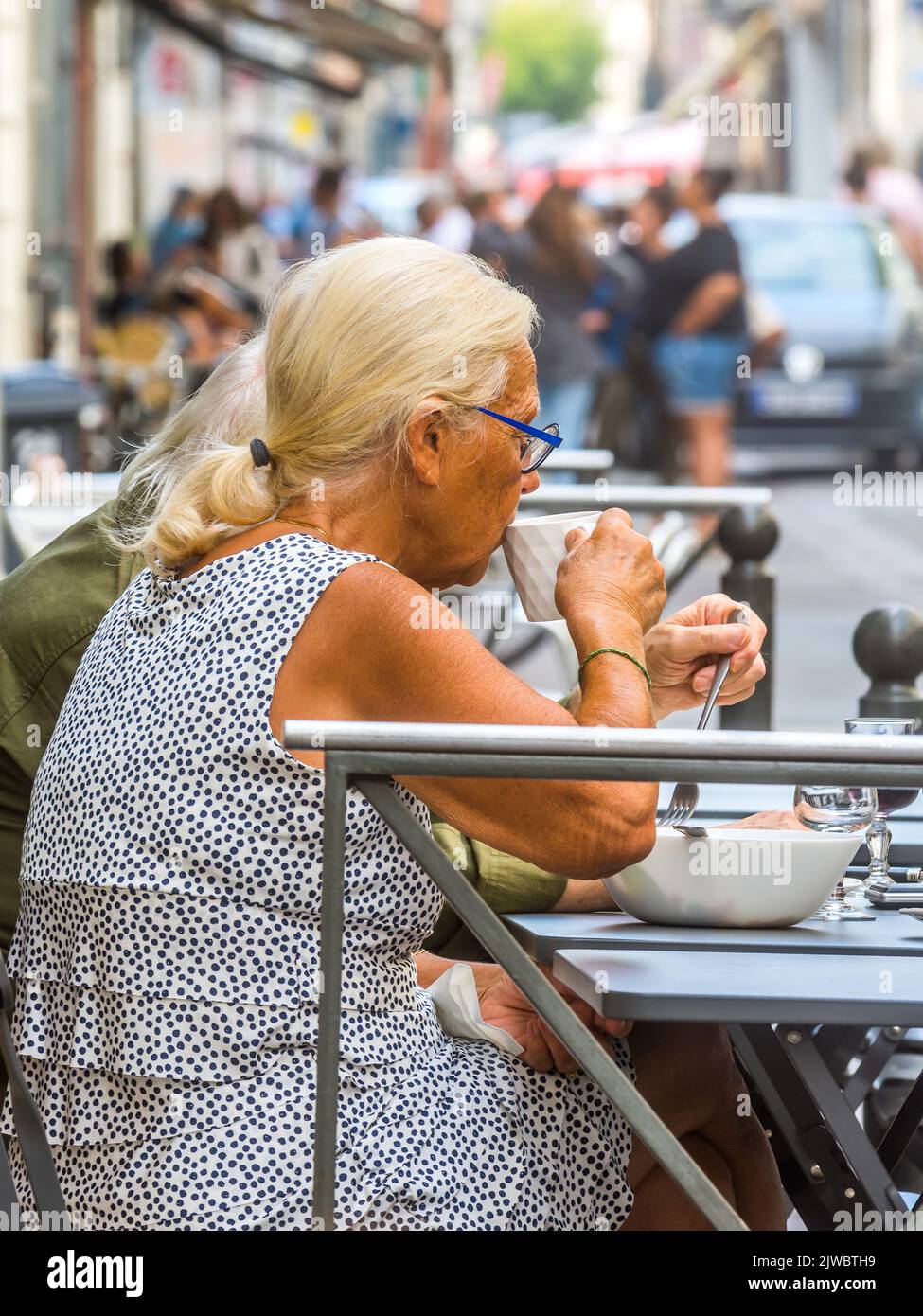 Reife Frau, die im Bistro im Freien auf der überfüllten Straße im Stadtzentrum - Tours, Indre-et-Loire (37), Frankreich isst und trinkt. Stockfoto