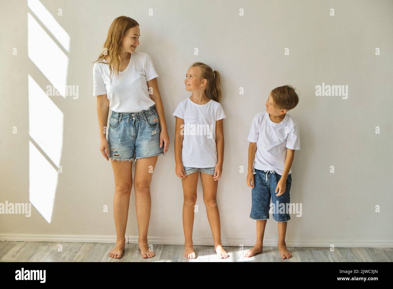 Mutter misst das Wachstum von Kindern zu einer Tochter und einem Sohn in der Nähe einer hellgrauen Wand Stockfoto