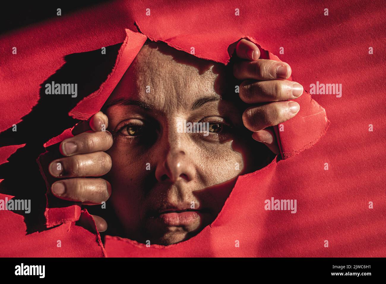 Porträt einer traurigen Frau, die durch ein Loch in Papier auf die Kamera schaut. Ich möchte freie Idee sein. Nahaufnahme Porträt einer verängstigten kaukasischen jungen Frau. Stockfoto