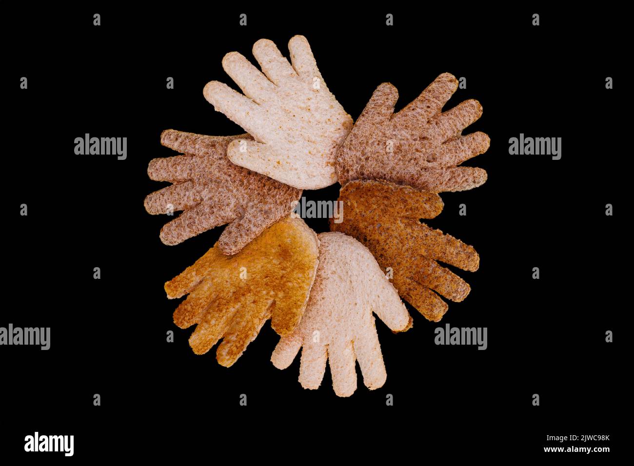 Multikulturelle Hände zusammen in einem Kreis aus geröstetem Brot auf schwarzem Hintergrund Stockfoto