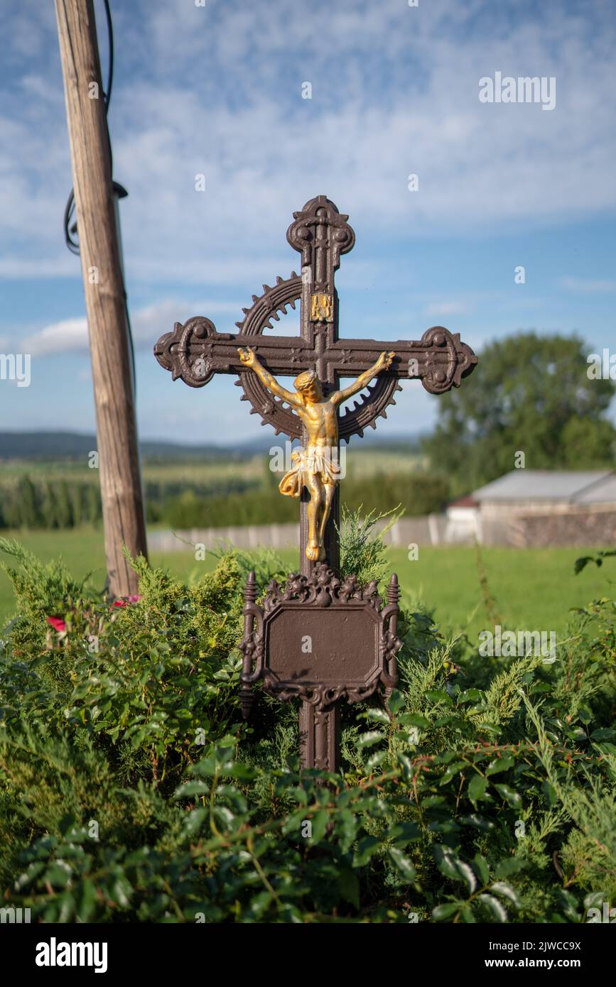 Teilweise beschädigt, aber renoviert Gusseisen Kreuzigungskreuz, ein typisches kleines Denkmal am Straßenrand in der tschechischen Landschaft. Stockfoto