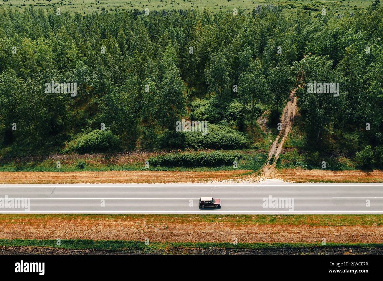 Altes Auto, das Gipskartonplatten auf dem Dach durch nicht-städtische Waldlandschaft transportiert, Luftaufnahme Stockfoto