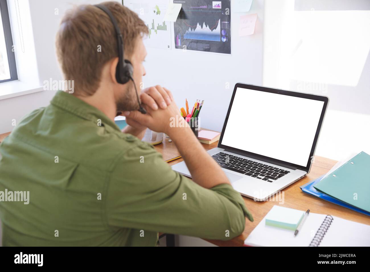 Mann, der im Büro ein Headset trägt und einen Laptop benutzt Stockfoto
