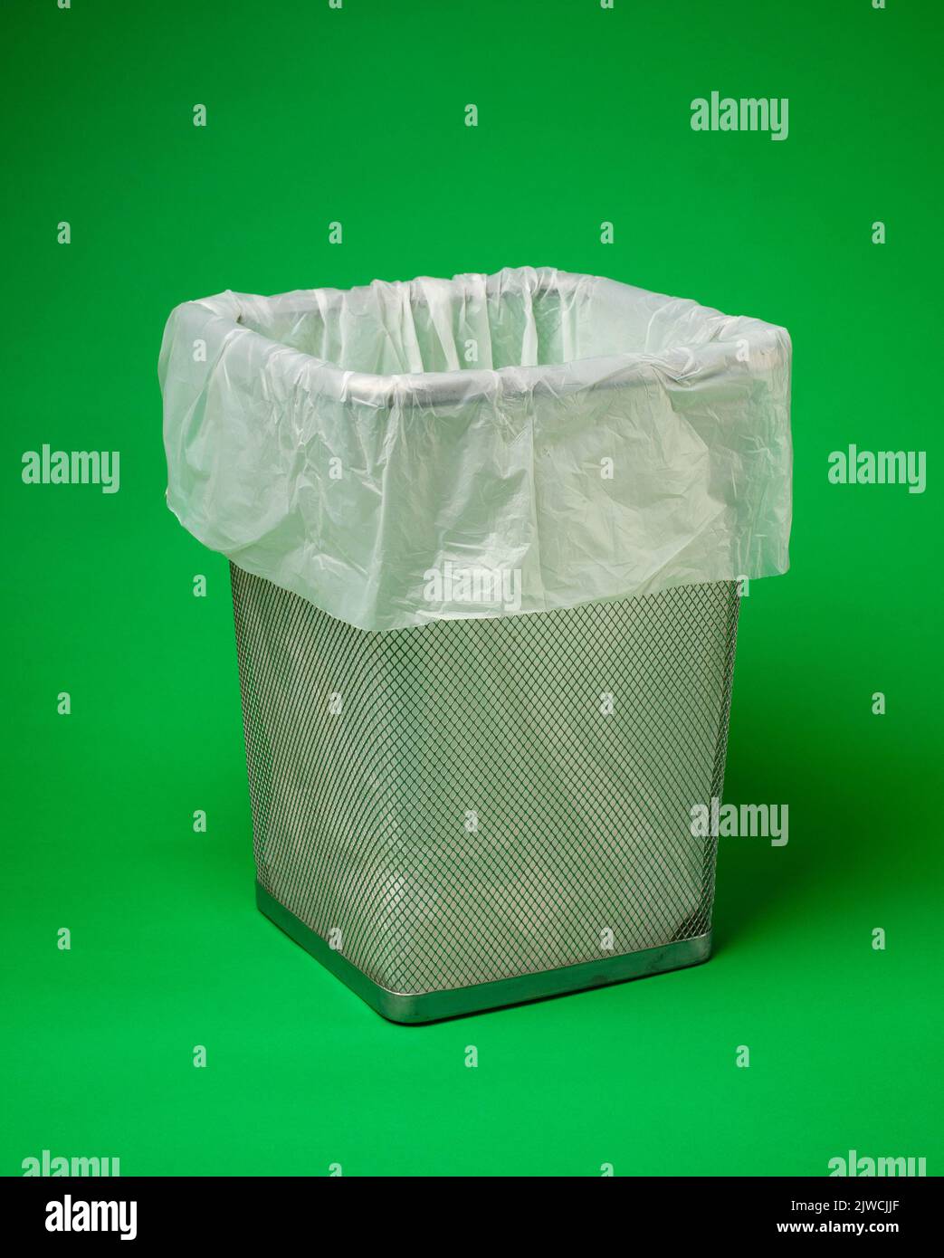 Leerer Metallabfallbehälter mit weißem, umweltfreundlichem, biologisch abbaubarem Müllbeutel steht auf grünem Hintergrund. Konzept für die Umweltsicherheit. Nahaufnahme Stockfoto