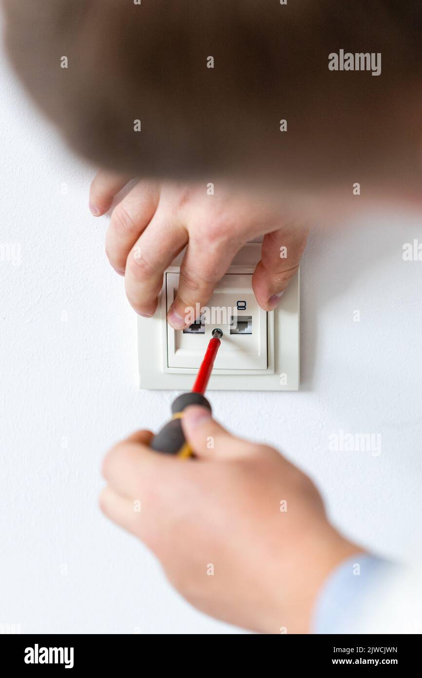 Installieren des Sockels aus nächster Nähe. Die Hände des Elektrikers ziehen die Schrauben in der Wandhalterung oder im Sockel mit einem Schraubendreher fest. Elektriker führt elektrische Arbeiten zu Hause durch Stockfoto