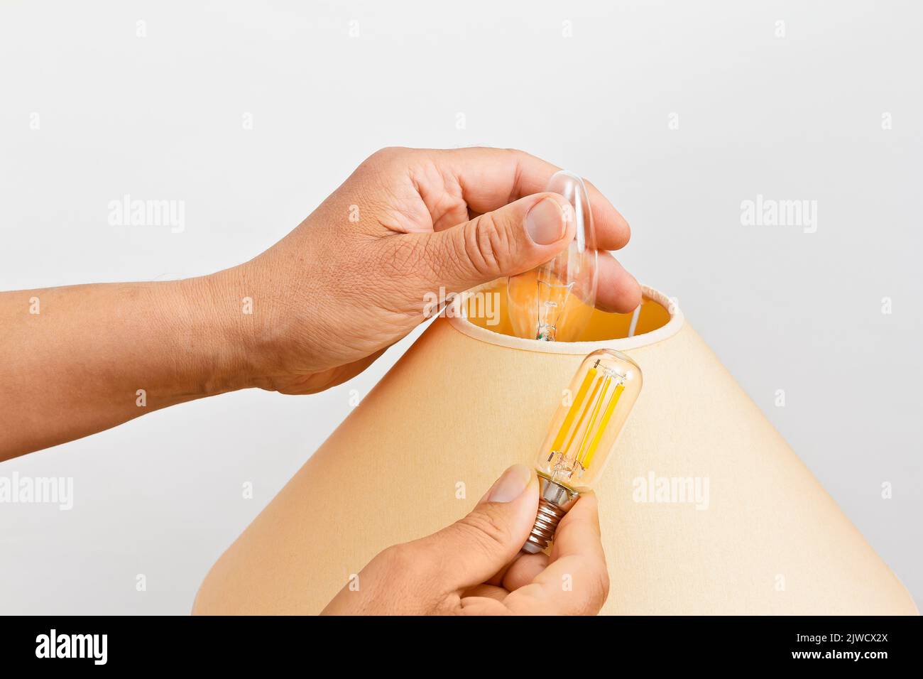 Stromsparkonzept: Nahaufnahme von männlichen Händen Austausch einer alten Glühbirne in einer Wohnzimmerlampe mit einer energieeffizienten LED-Glühfaden-Version. Stockfoto