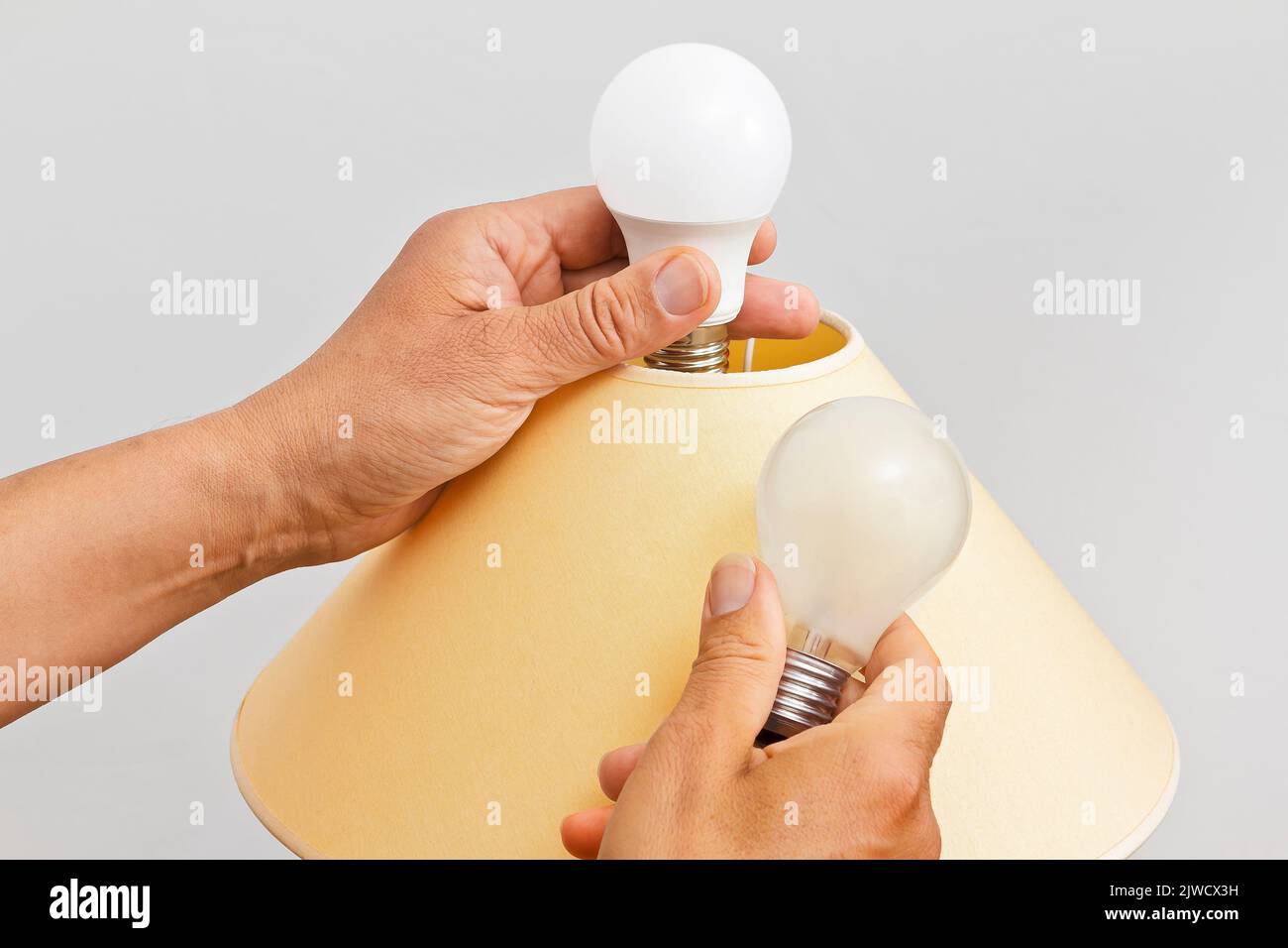 Konzept zur Beendigung von Energieverschwendung: Nahaufnahme von männlichen Händen, die eine alte Glühbirne in einer Wohnzimmerlampe durch eine energieeffiziente LED-Version austauschen. Stockfoto