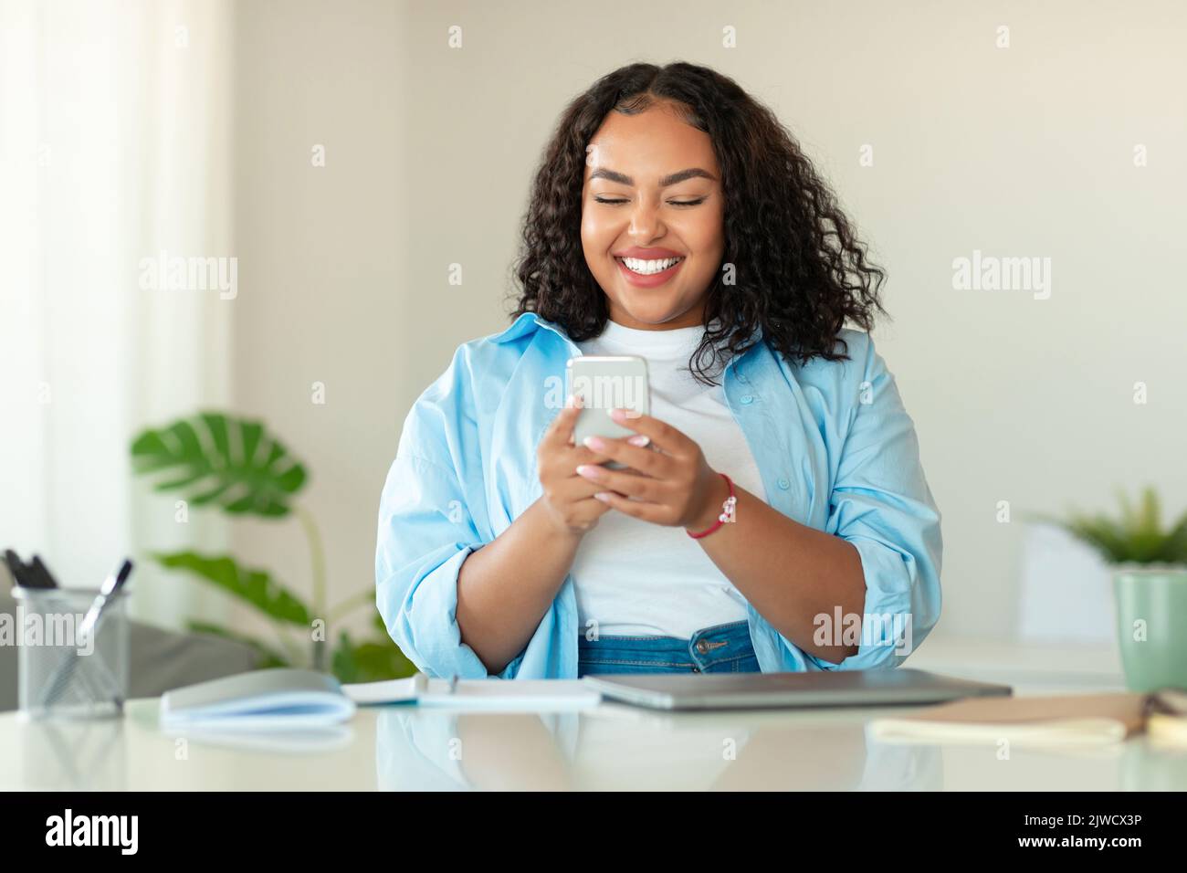 Glückliche Schwarze Frau Mit Mobiltelefon Sitzen In Modernen Büro Stockfoto