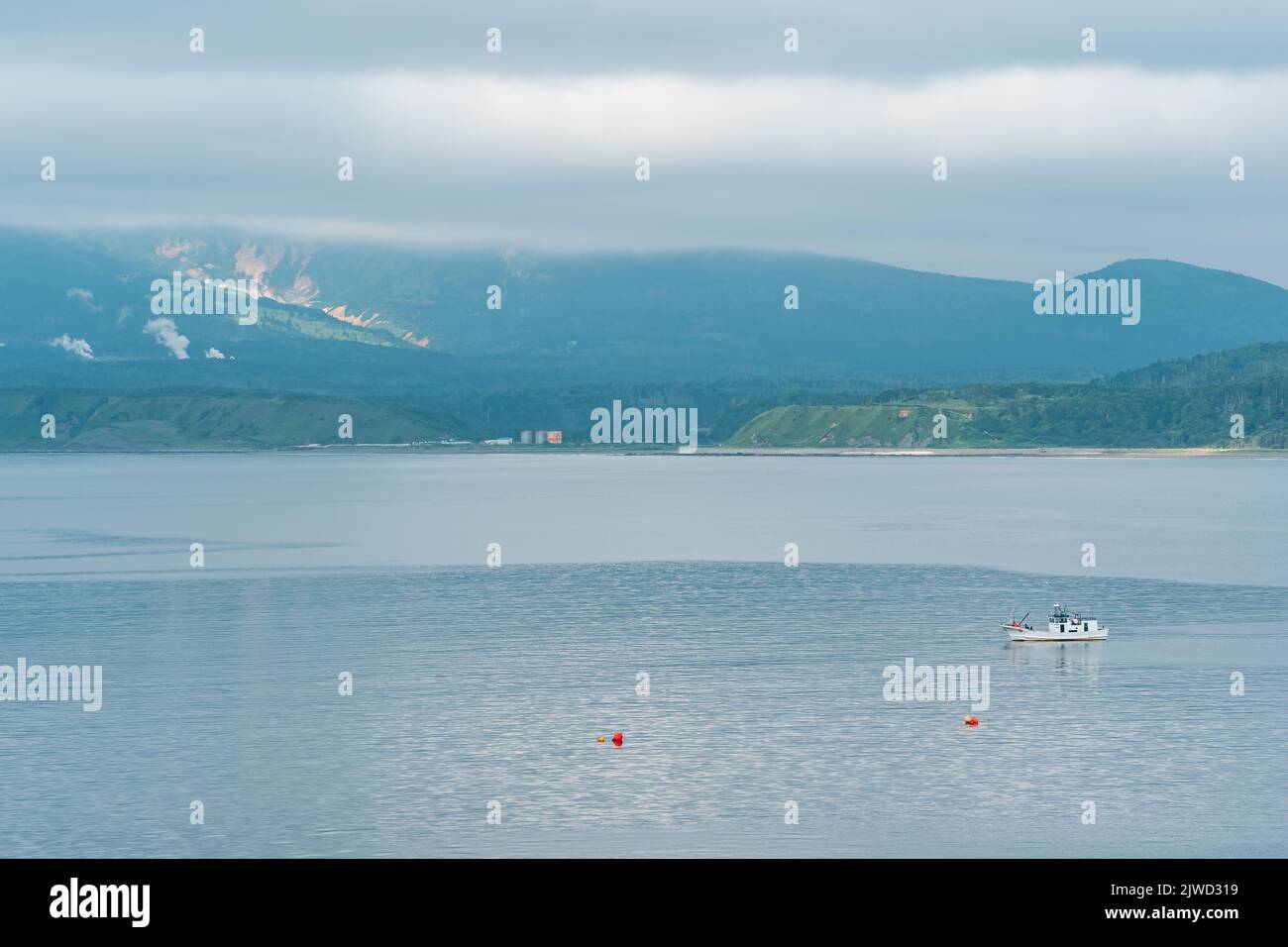 Meeresbucht mit nebligen Bergen im Hintergrund, Blick auf den Mendelejew-Vulkan an einem bewölkten Tag Stockfoto