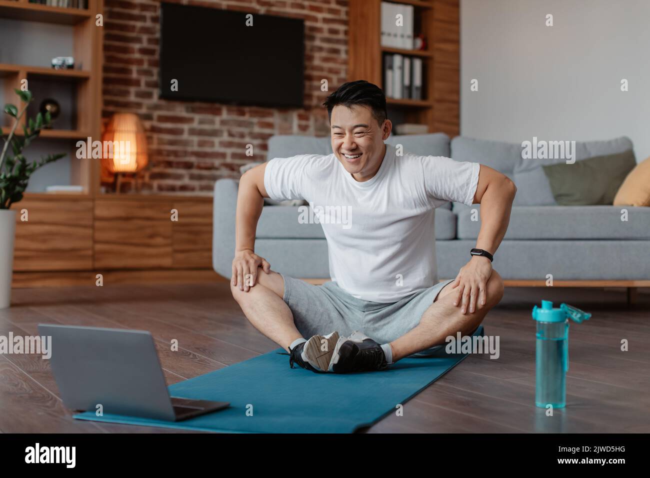 Inländisches Trainingskonzept. Reifer asiatischer Mann praktiziert Yoga mit Online-Lehrer auf Laptop, so dass Schmetterling Asana Stockfoto