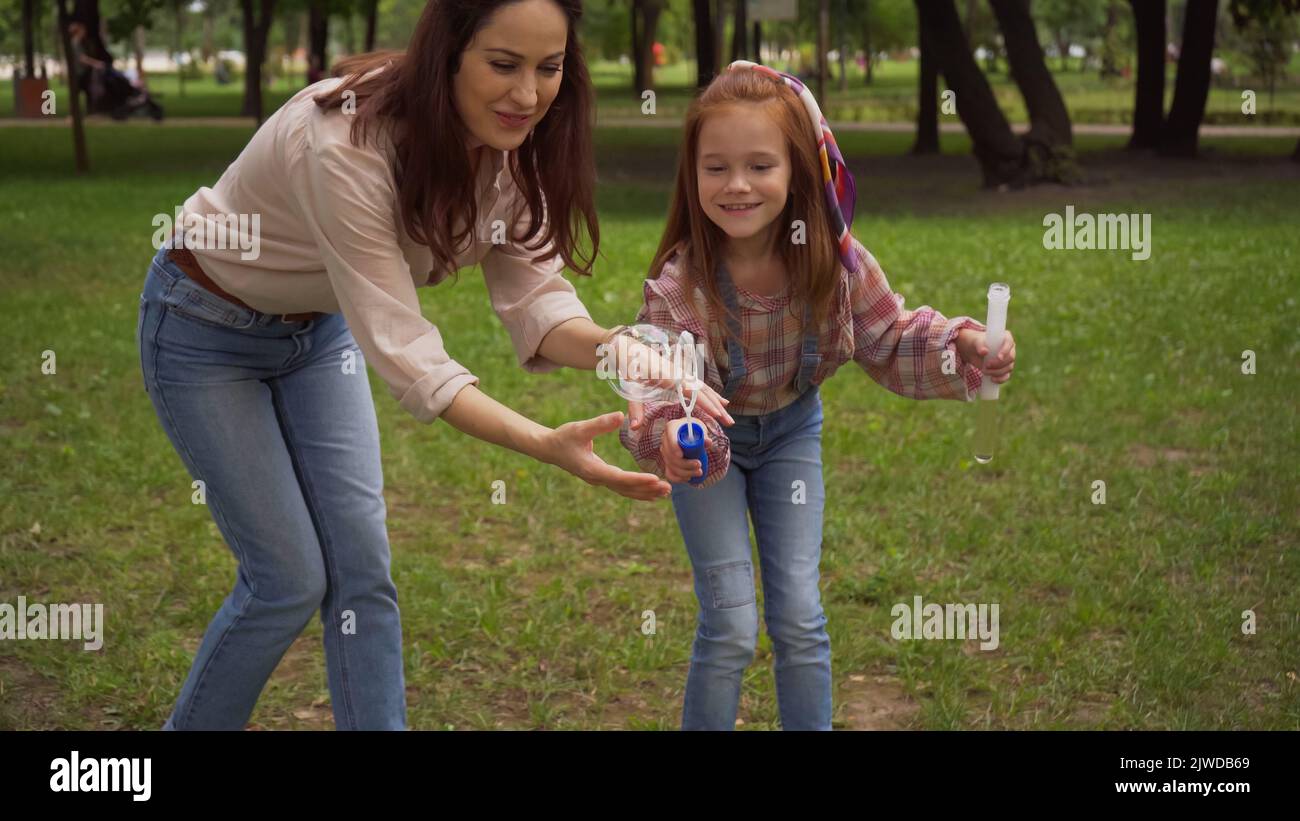 Lächelnde Eltern und Mädchen halten Seifenblasen im Sommerpark, Stock Bild Stockfoto