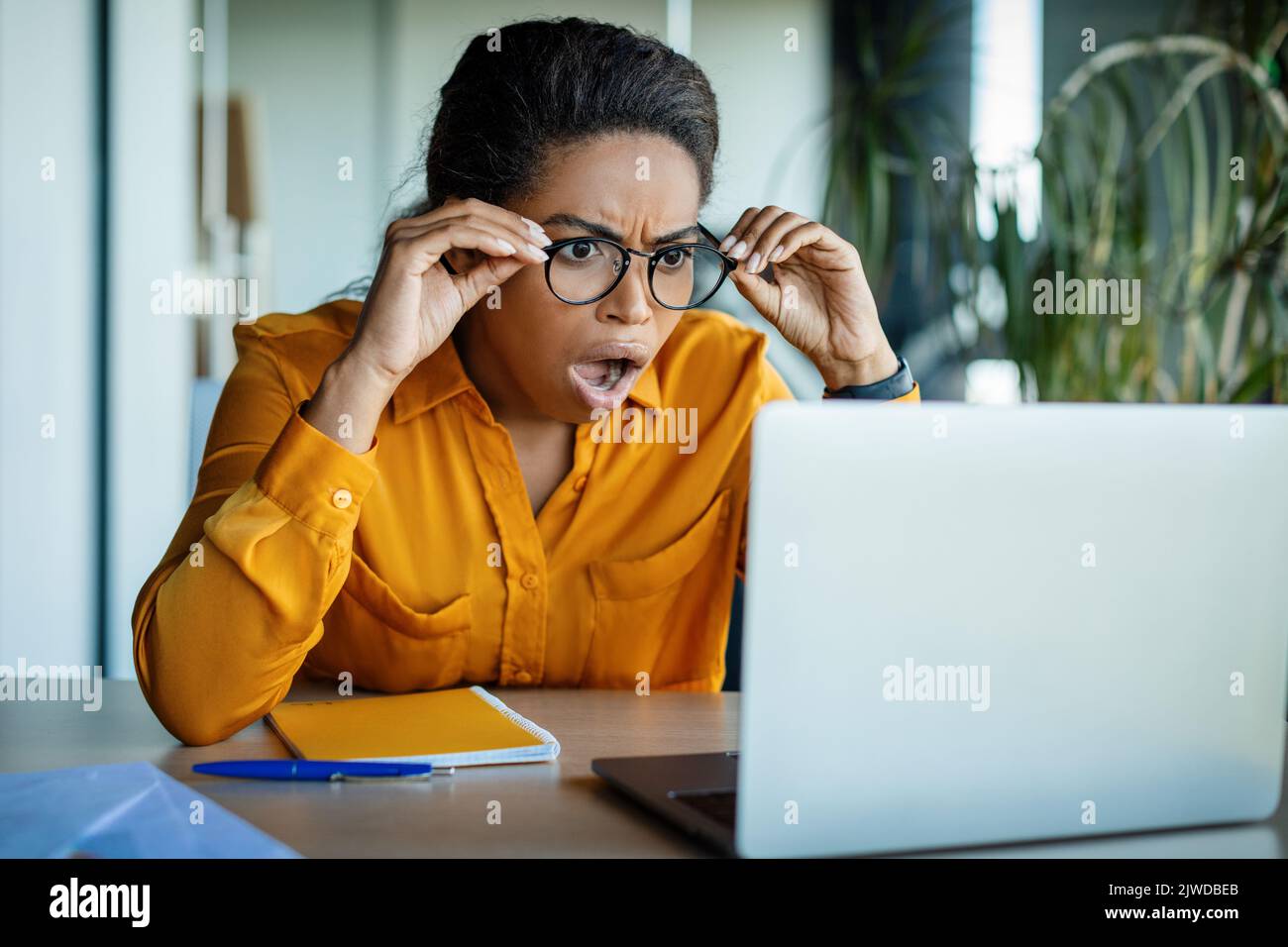 Schockierte schwarze Geschäftsfrau, die mit offenem Mund auf den Laptop-Bildschirm schaut und schockierende Geschäftsnachrichten liest Stockfoto
