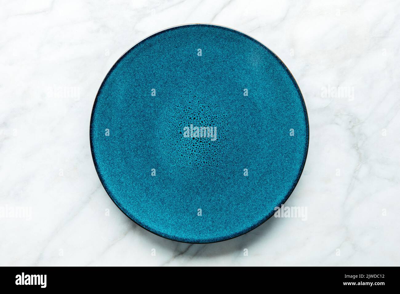 Eine blaue Platte, von oben auf weißem Marmorboden aufgenommen. Modernes Geschirr Stockfoto