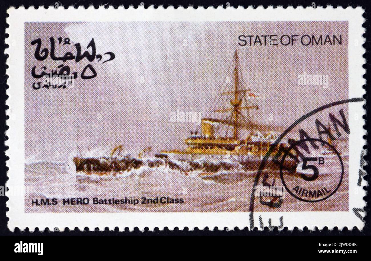 OMAN - UM 1977: Eine im Bundesstaat Oman gedruckte Briefmarke zeigt HMS Hero, das zweite und letzte Schlachtschiff der Eroberer-Klasse, das als Eisenschmiede diente Stockfoto