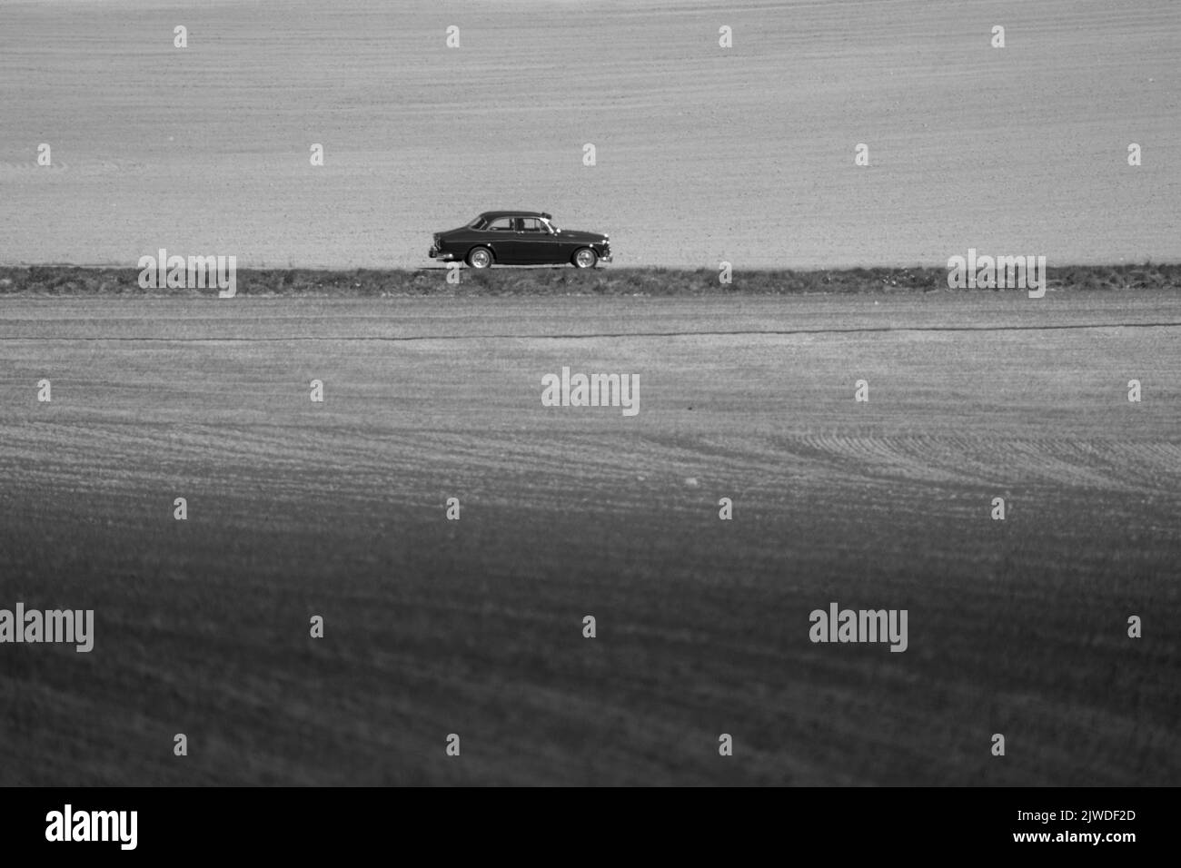 Eine Graustufe eines Retro-Autos, das die verlassene Straße entlang fährt Stockfoto