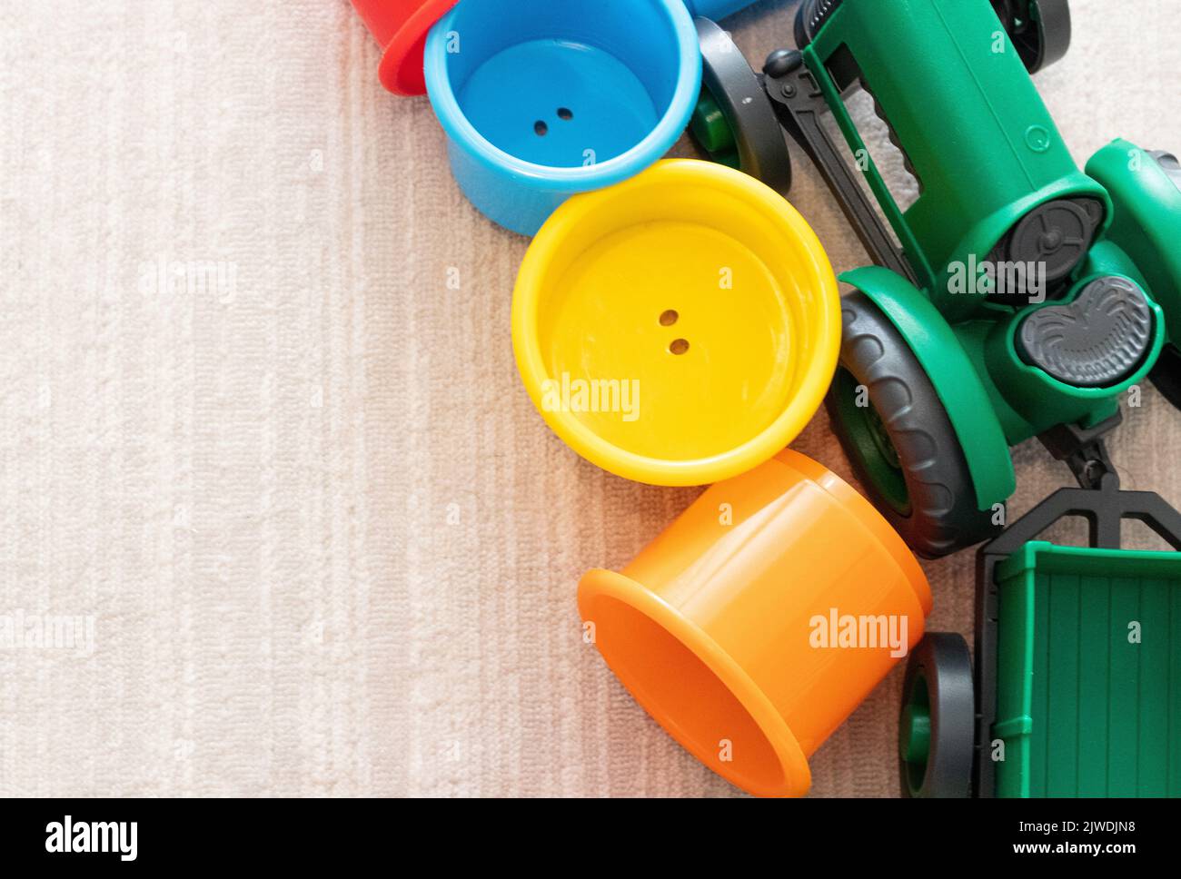 Baby oder Kinder Spielzeug Hintergrund. Draufsicht auf bunte Spielzeuge. Grüner Traktor und Plastikbecher in verschiedenen Farben. Verrauschtes und horizontales Foto. Keine Personen. Stockfoto