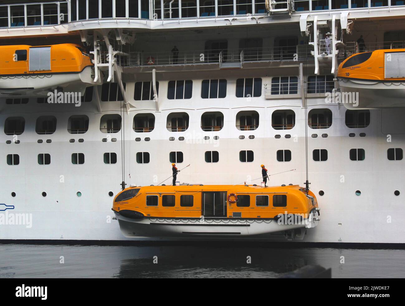 Riesiges Kreuzschiff, das von Männern gereinigt wird, die auf Rettungsschiffen balancieren, die an der Seite aufgehängt sind Stockfoto