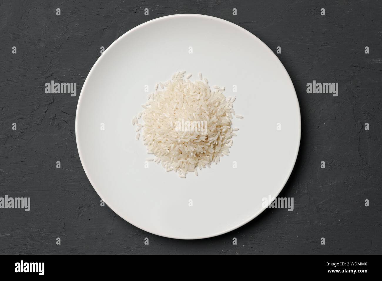 Haufen von trockenem Reis in einer Schüssel auf schwarzem Hintergrund, Mangel an Nahrung, Hunger-Konzept Stockfoto